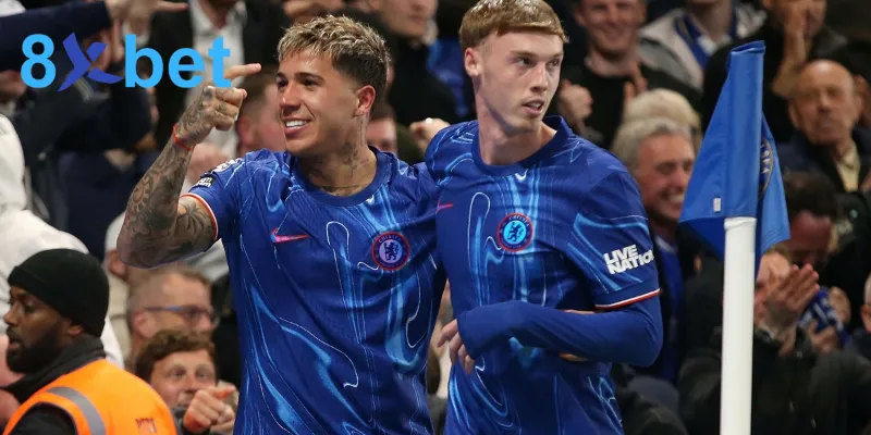 Ảnh 8xbet media chụp hai cầu thủ Chelsea áo xanh ăn mừng trên sân, góc trái có logo 8xbet