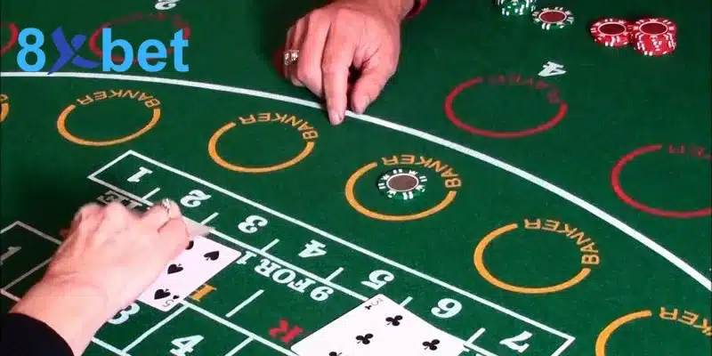 Bàn baccarat nỉ xanh với các ô cược Banker, phỉnh và lá bài đang được chia, minh họa luật baccarat sicbo roulette