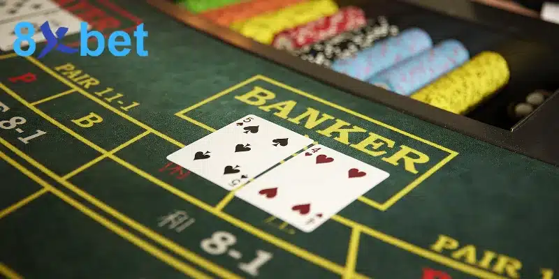 Hai lá 5 bích và 4 cơ nằm trên ô Banker của bàn nỉ xanh, minh họa cách chơi baccarat khi đặt cửa