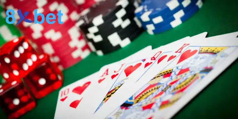 Các lá 10, J, Q, K và A cơ cạnh xúc xắc đỏ và chồng chip, minh họa cách chơi baccarat với lá bài 0 điểm