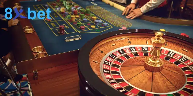 Bàn đặt cược roulette nỉ xanh dương có chip trên các ô số, tay dealer và bánh xe phía trước