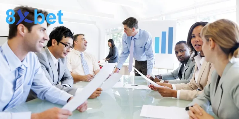 Nhân viên văn phòng họp quanh bàn kính cạnh biểu đồ cột, minh họa đội ngũ sau các đối tác chiến lược của 8xbet