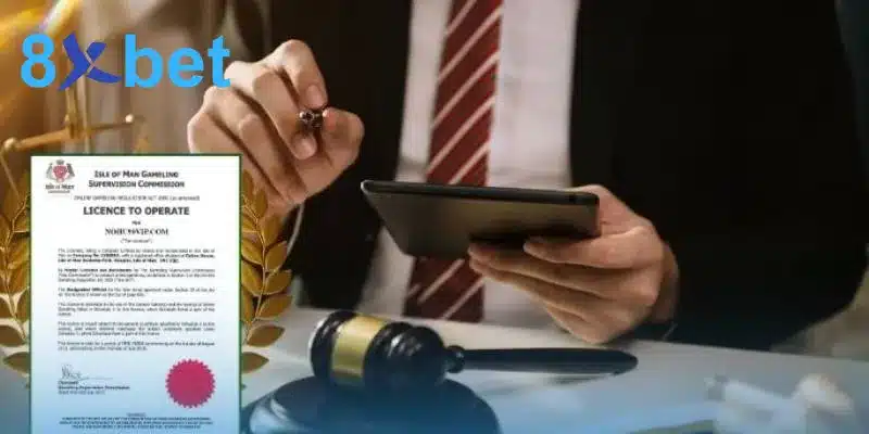 Mẫu giấy phép hoạt động Licence to Operate của Isle of Man cạnh búa thẩm phán và người mặc vest cầm máy tính bảng