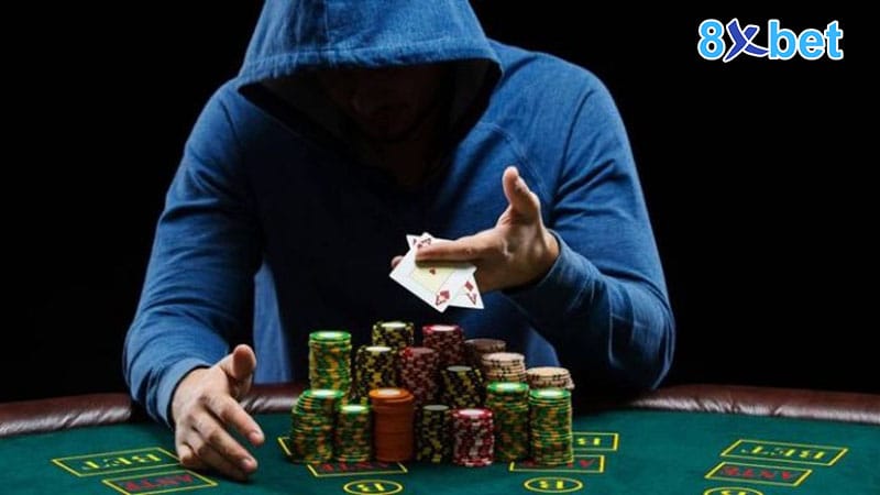 Người chơi poker 8xbet mặc áo trùm đầu lật hai lá bài và đẩy chồng chip trên bàn