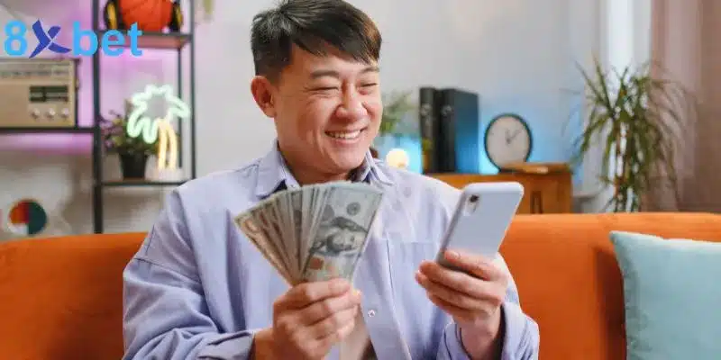 Người đàn ông cầm điện thoại và xấp tiền, mỉm cười khi xem kết quả keno trực tiếp