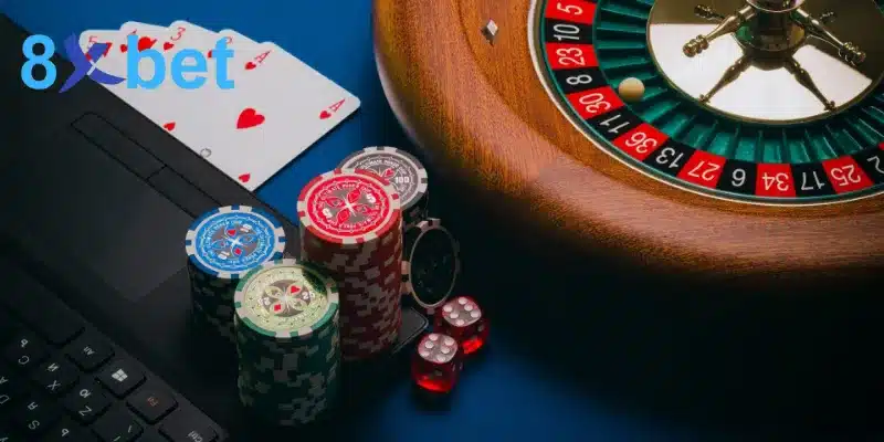 Bánh xe roulette gỗ, chồng phỉnh, bộ bài và xí ngầu cạnh laptop, minh họa trò baccarat sicbo roulette online