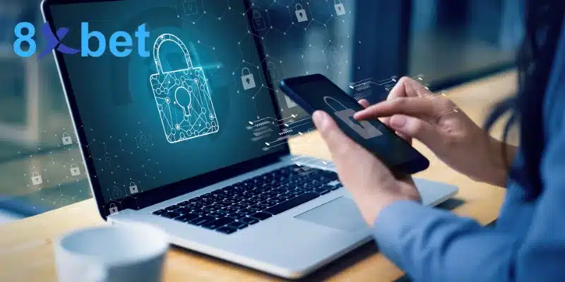 Laptop hiển thị ổ khóa kỹ thuật số và tay cầm điện thoại, minh họa bảo vệ tài khoản cá cược trên nhiều thiết bị