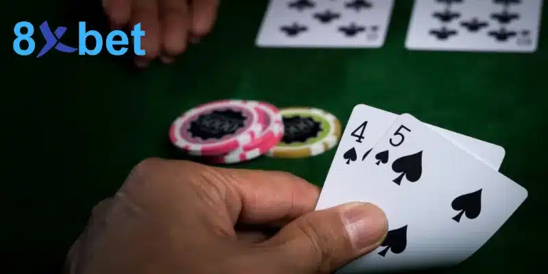 Bàn tay cầm hai lá 4 bích và 5 bích cạnh chồng chip, ví dụ cách chơi baccarat với tay bài 9 điểm