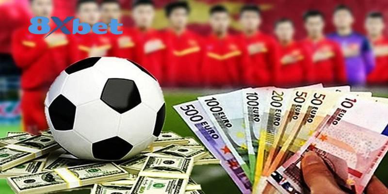 Đội hình dự kiến minh họa bằng hàng cầu thủ áo đỏ đứng chào cờ phía sau quả bóng và xấp tiền giấy